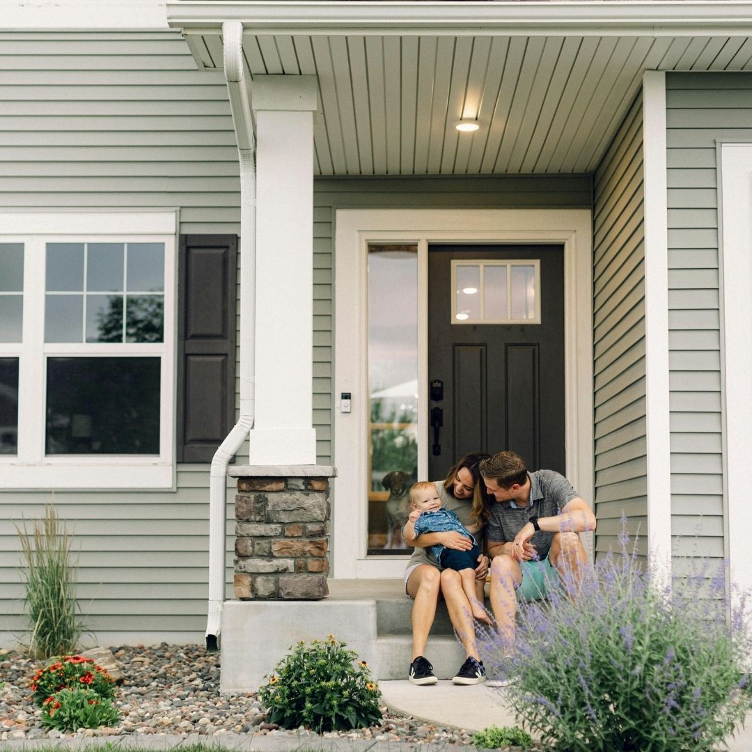 A happy family with a small child sitting together on the front steps of their home.