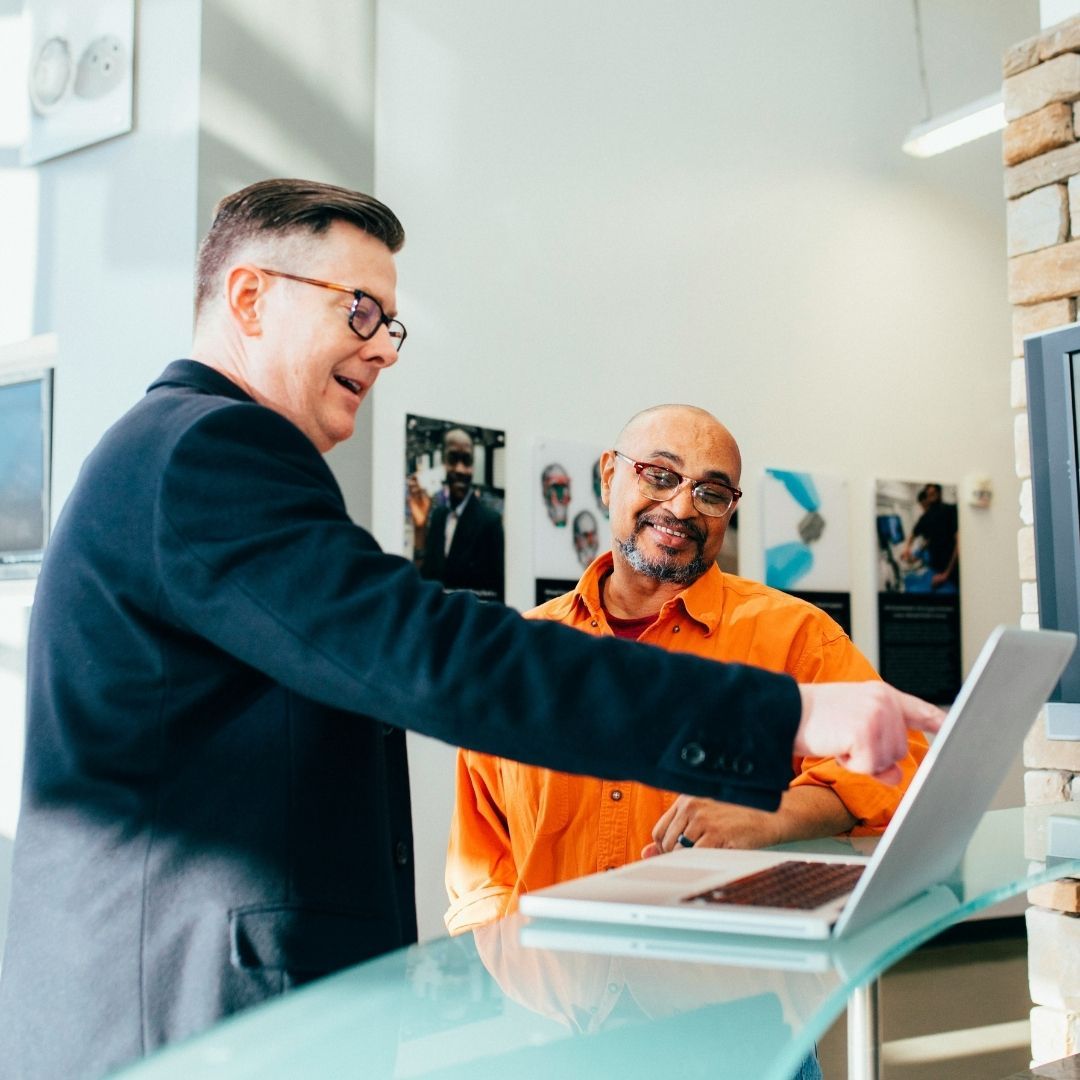 A financial consultant pointing to a laptop screen while explaining foreclosure options to a client.