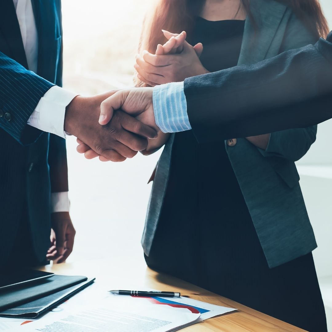 Two people shaking hands over documents on a desk, symbolizing a business agreement or partnership.