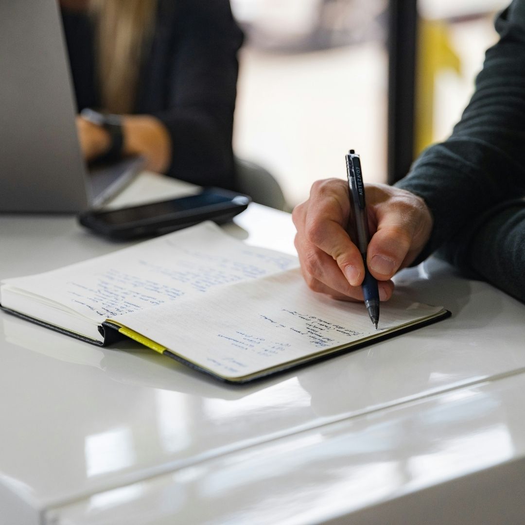 A person's hand writing notes in a notebook during a consultation.