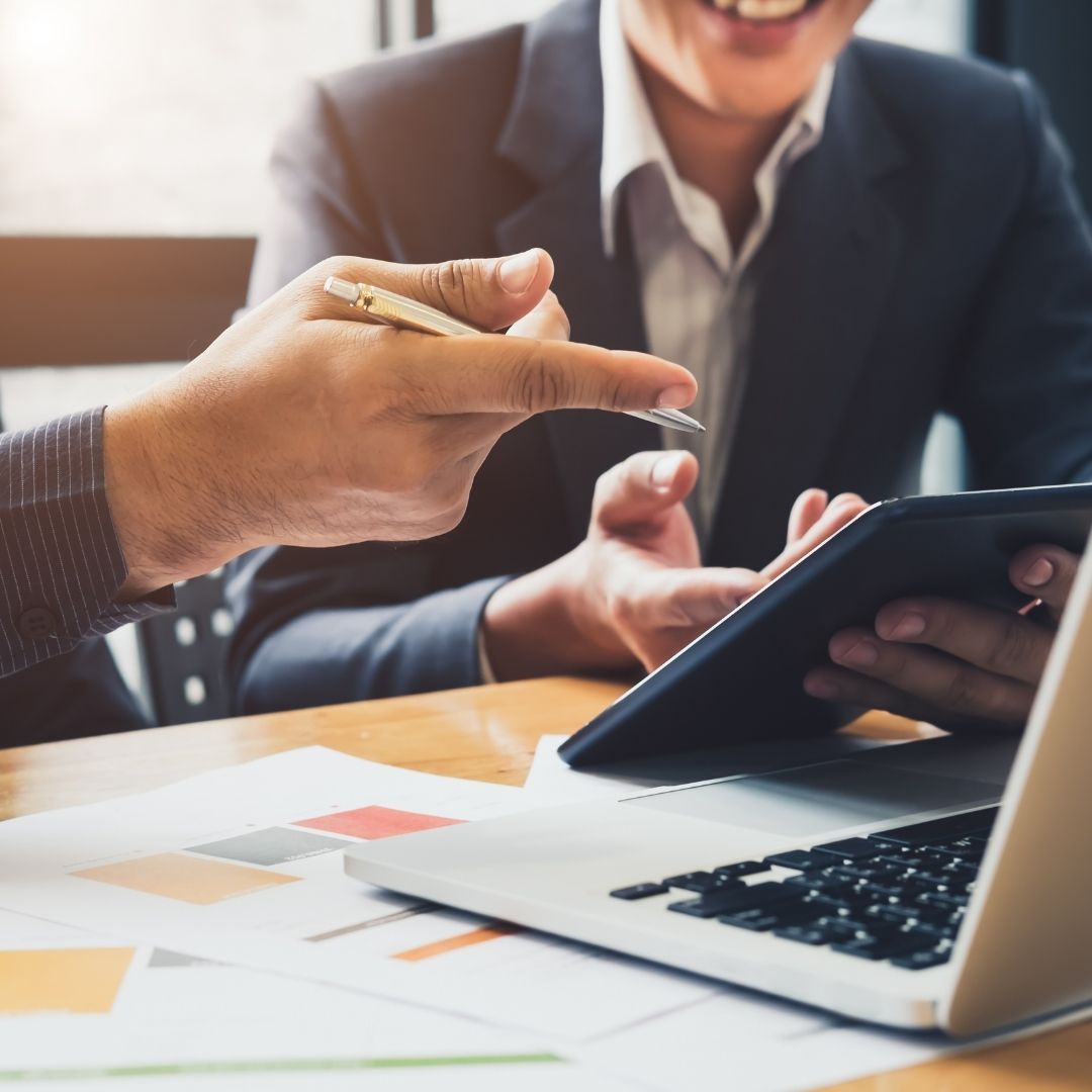 Two professionals discussing plans using a tablet and a laptop.