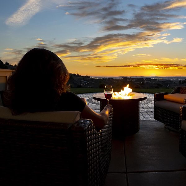 Woman sitting on her patio with a fire pit holding a glass of wine in the evening