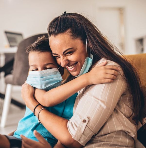 A mother and son in masks hugging