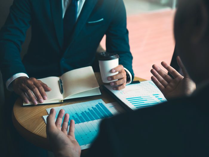 Two businessmen discussing a financial planning graph and company financials at a small round table.