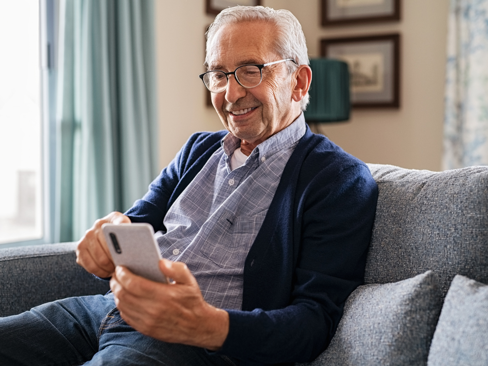 A older man looking at his smartphone while he sits on his couch