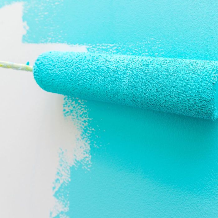 A brush being used to paint a blue wall