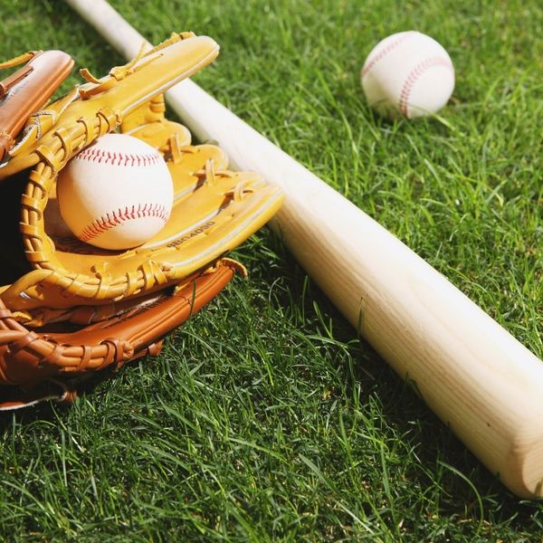 Baseball mitts, balls, and a bat laying in the grass