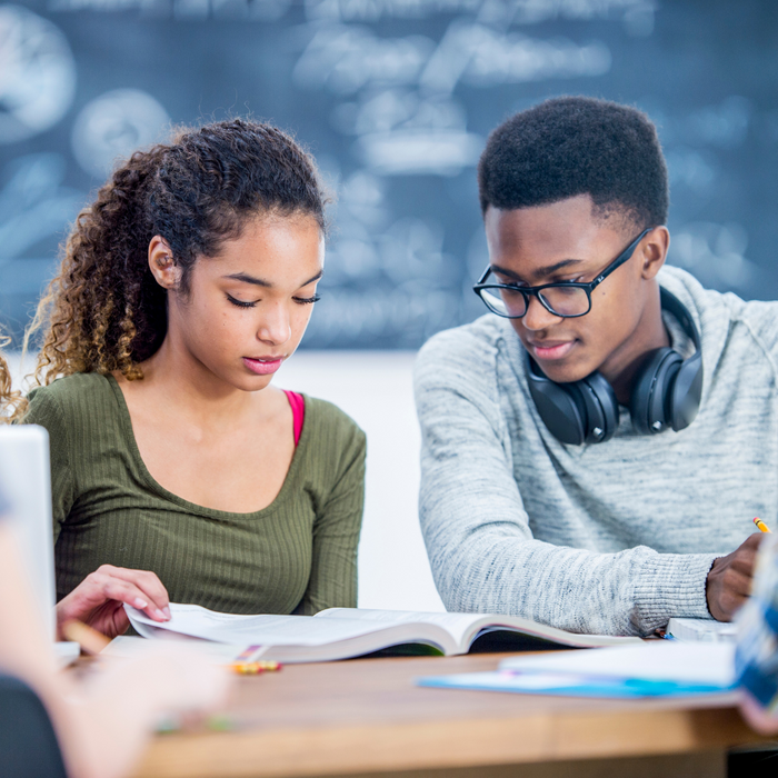 two students reading a book together. 