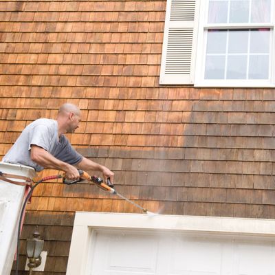 a professional in a cherry picker power washing house siding