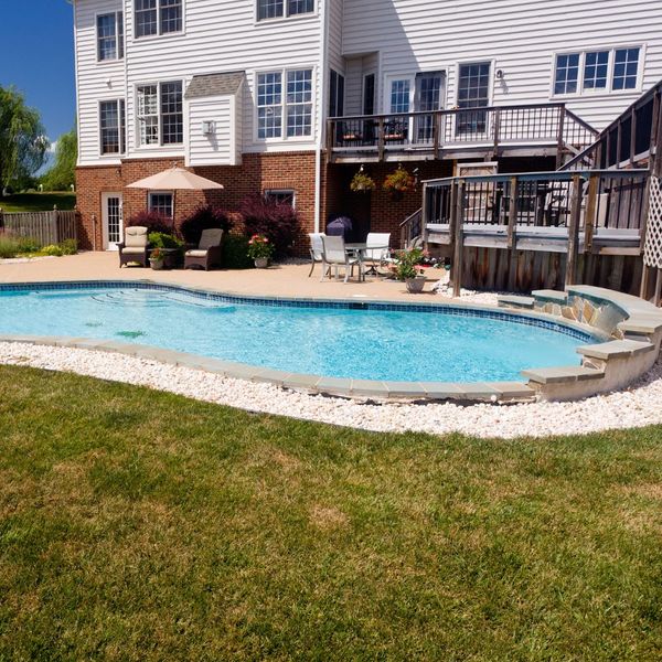 backyard pool next to white and brick house with wood deck