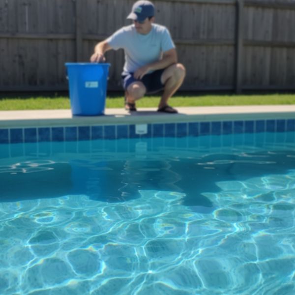 A person performing a bucket test for a pool leak. A person performing a bucket test for a pool leak.