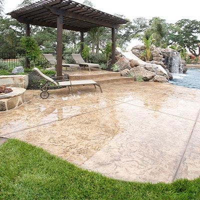 Image of a backyard with a pool with a waterfall and chairs by the pool 