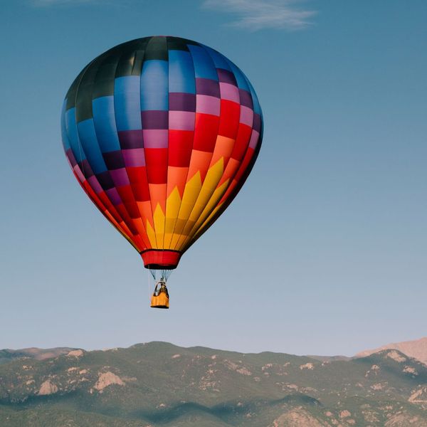 a rainbow hot air balloon flying over mountains