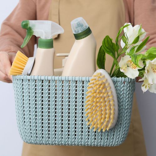 Person holds blue wicker bucket with cleaning supplies and flowers