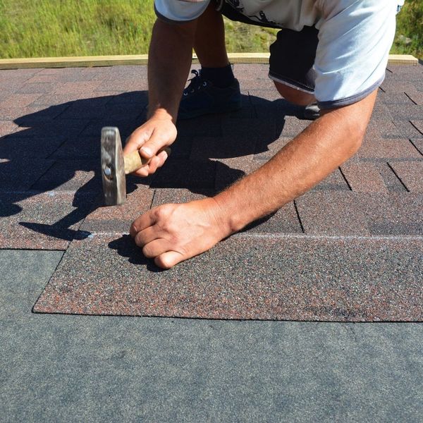 hammering asphalt shingles on roof