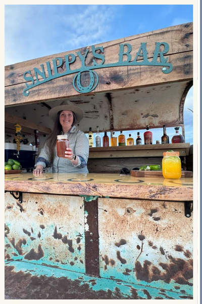 A smiling bartender serving a drink in a mason jar from a mobile bar called "Snippy's Bar" A smiling bartender serving a drink in a mason jar from a mobile bar called "Snippy's Bar"