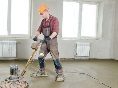 Construction worker operating power trowel machine during concrete floor wet grinding process by electrical grinder.