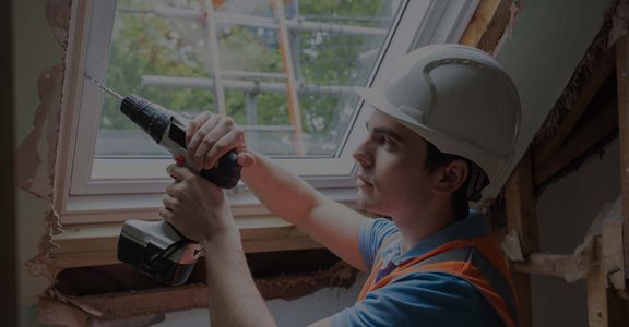 oung construction worker installs replacement window in attic.