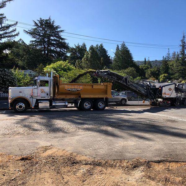 Asphalt milling machine grinding pavement and loading it directly into a Durden Construction dump truck.