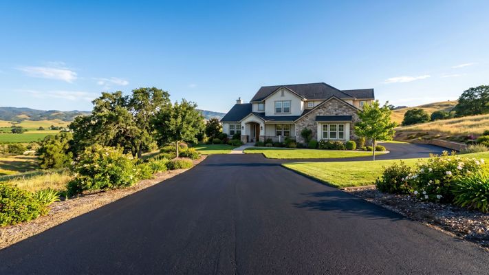 A wide-angle view of a new black asphalt driveway at a San Benito County home with beautiful landscaping.