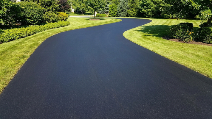 Flawlessly finished black asphalt driveway curving through lush landscaped residential lawn.