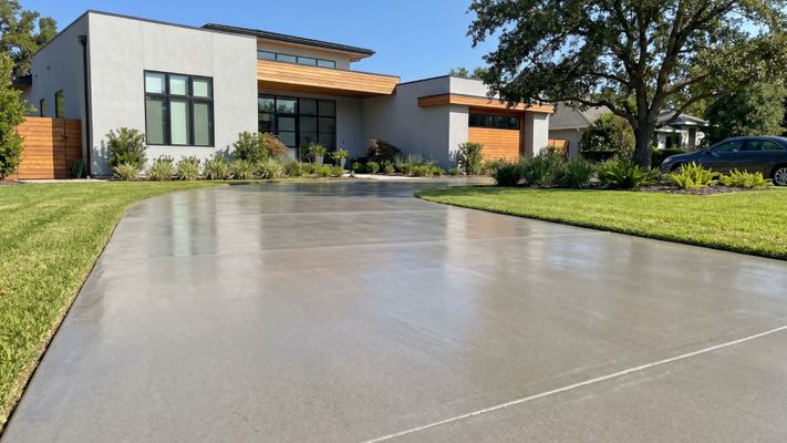 Freshly sealed residential concrete driveway outside a modern home under sunny skies.