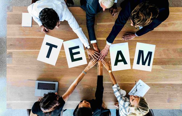 Image of a group of people putting their hand together over the word team