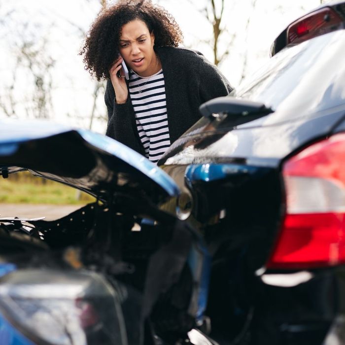woman on the phone while looking at damage from a minor car accident