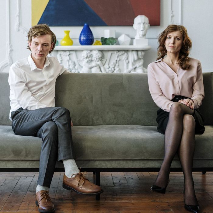 well-dressed couple sitting at opposite ends of long couch looking dour