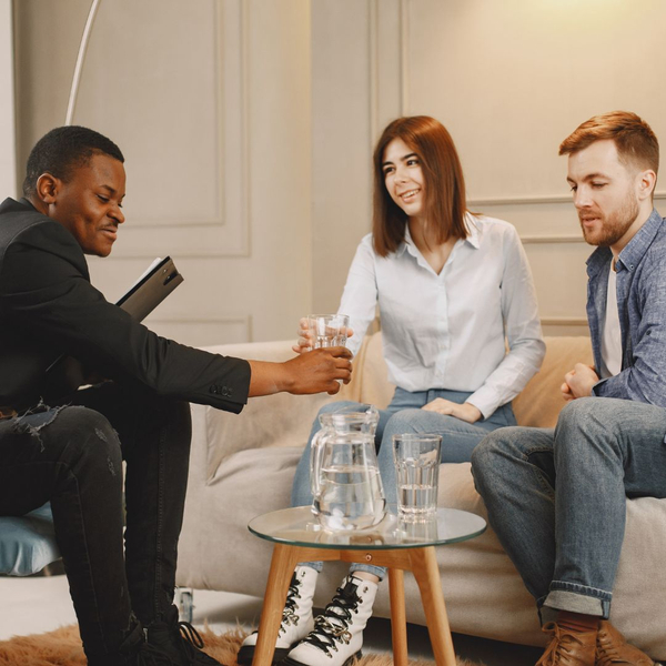 two people sitting for a meeting with a third party holding a clipboard