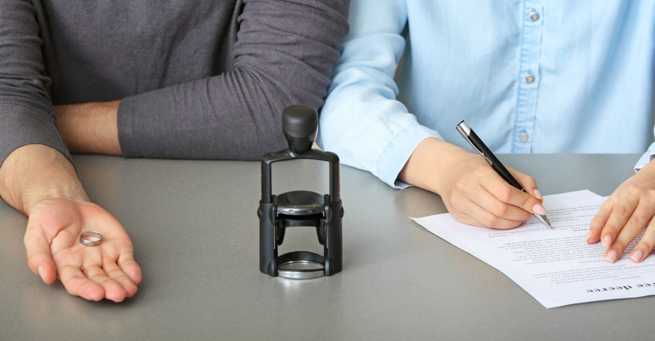 a person holding a ring out and another signing paperwork in front of an official stamp