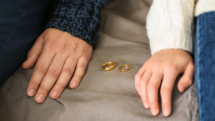 Man and woman rest their hands with wedding rings between them