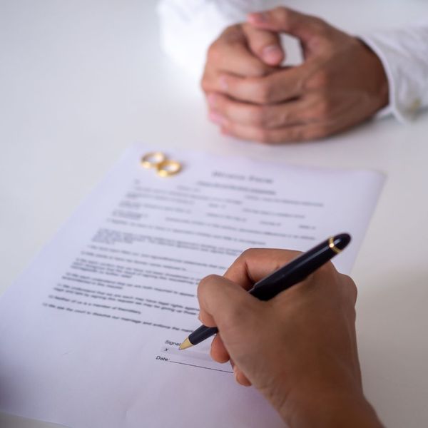 a person signing paperwork with two wedding rings sitting on the papers