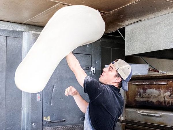 Man hand-tossing large pizza dough in the air
