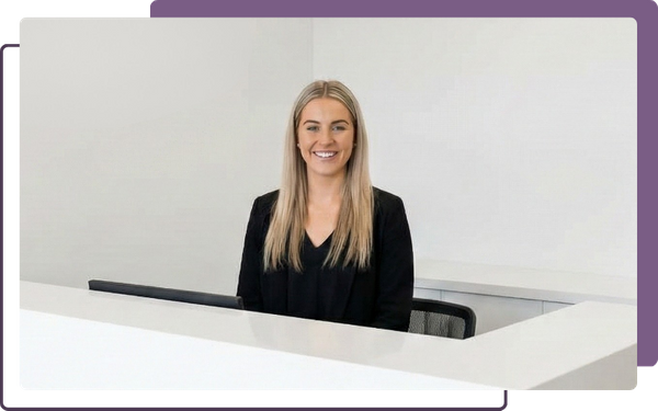 A welcoming reception area at Infinite Health Chiropractic, featuring a smiling receptionist at a modern desk with the clinic's logo on the wall behind her.