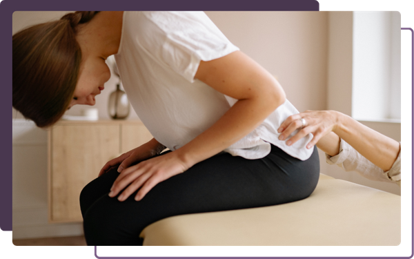 chiropractor gently guiding/feeling patient's lower back as she bends over