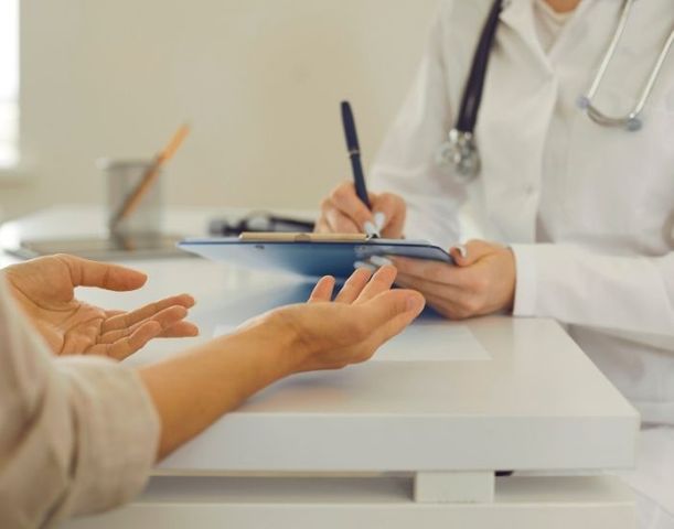 Close-up of a doctor in a white coat with a stethoscope, writing on a clipboard during a patient consultation