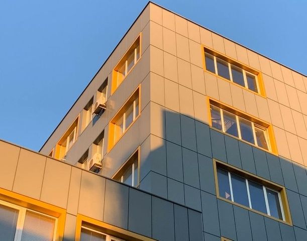 A low-angle shot of a modern apartment or office building with yellow accents against a clear blue sky, representing commercial property insurance.