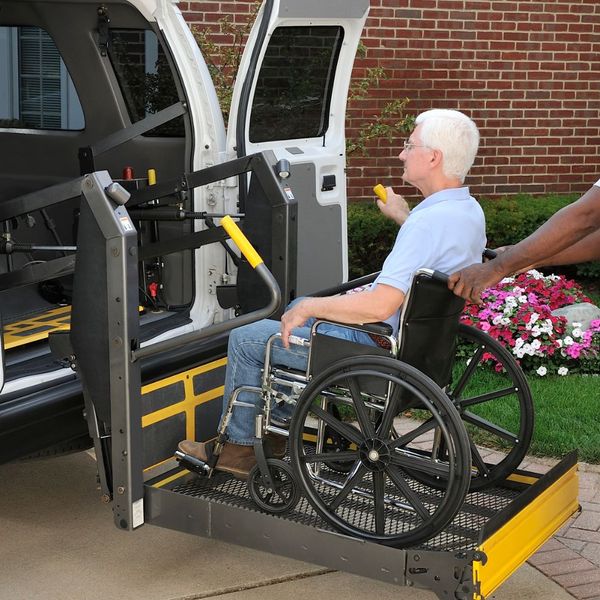 Man in a wheelchair being hoisted into a van. 