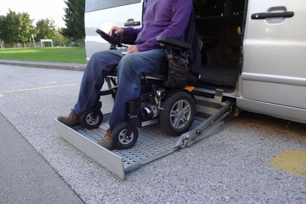 man in an electric wheelchair being raised into or lowered from a special needs vehicle