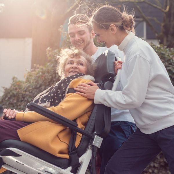 Two people surrounding a patient in a wheelchair. 