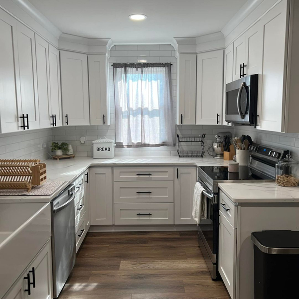 Traditional U-shaped kitchen featuring white shaker cabinets, dark hardware, and a small window above the sink.