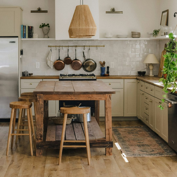 Bohemian-style kitchen with light cream cabinets, open shelving, a wooden farmhouse table island, and copper pots hanging on the backsplash.