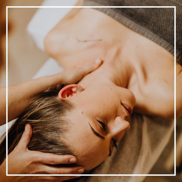A beautiful close-up of a woman with her eyes closed, resting her head on a massage table next to a small bowl and a yellow flower, capturing a moment of deep relaxation.
