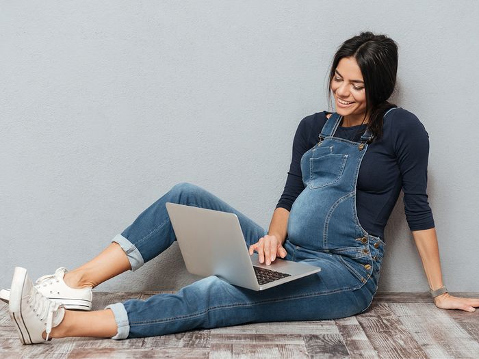 Pregnant woman in overalls looking at computer