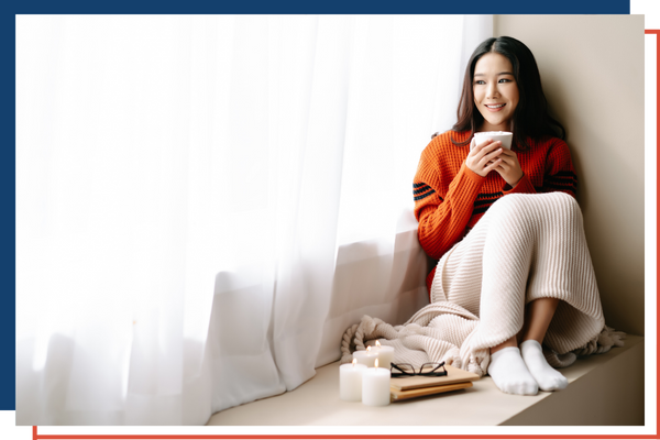 A women cozied up by a window enjoying coffee