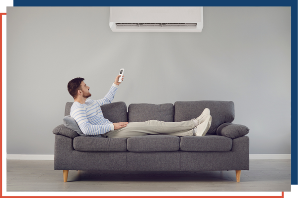 A man sitting on a couch using a remote to activate his AC