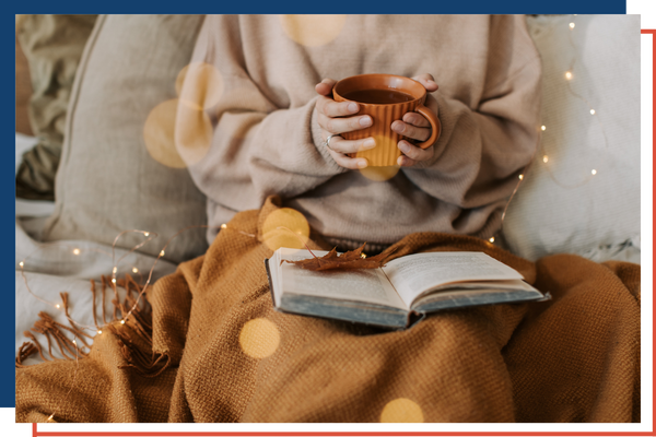 Woman reading a book cozy under a blanket with a hot cocoa