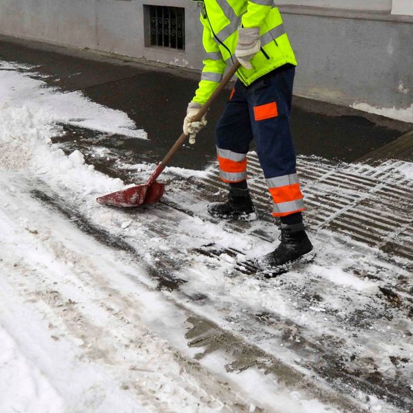 Worker using a snow shovel in front of a commercial building