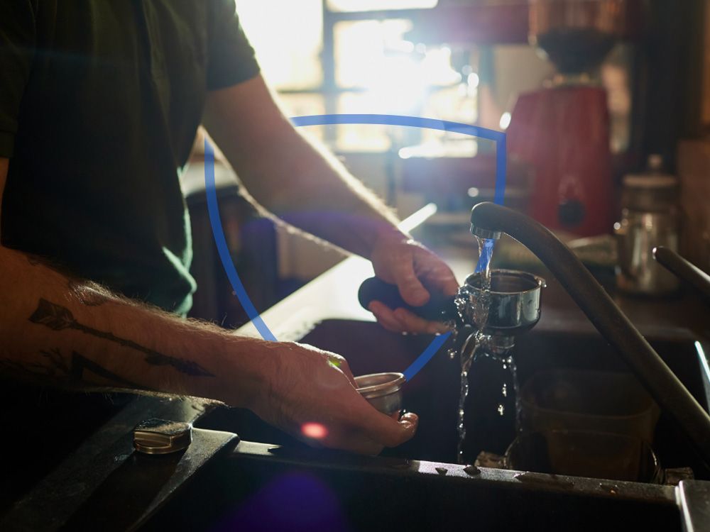 Barista cleaning espresso machine parts in sink